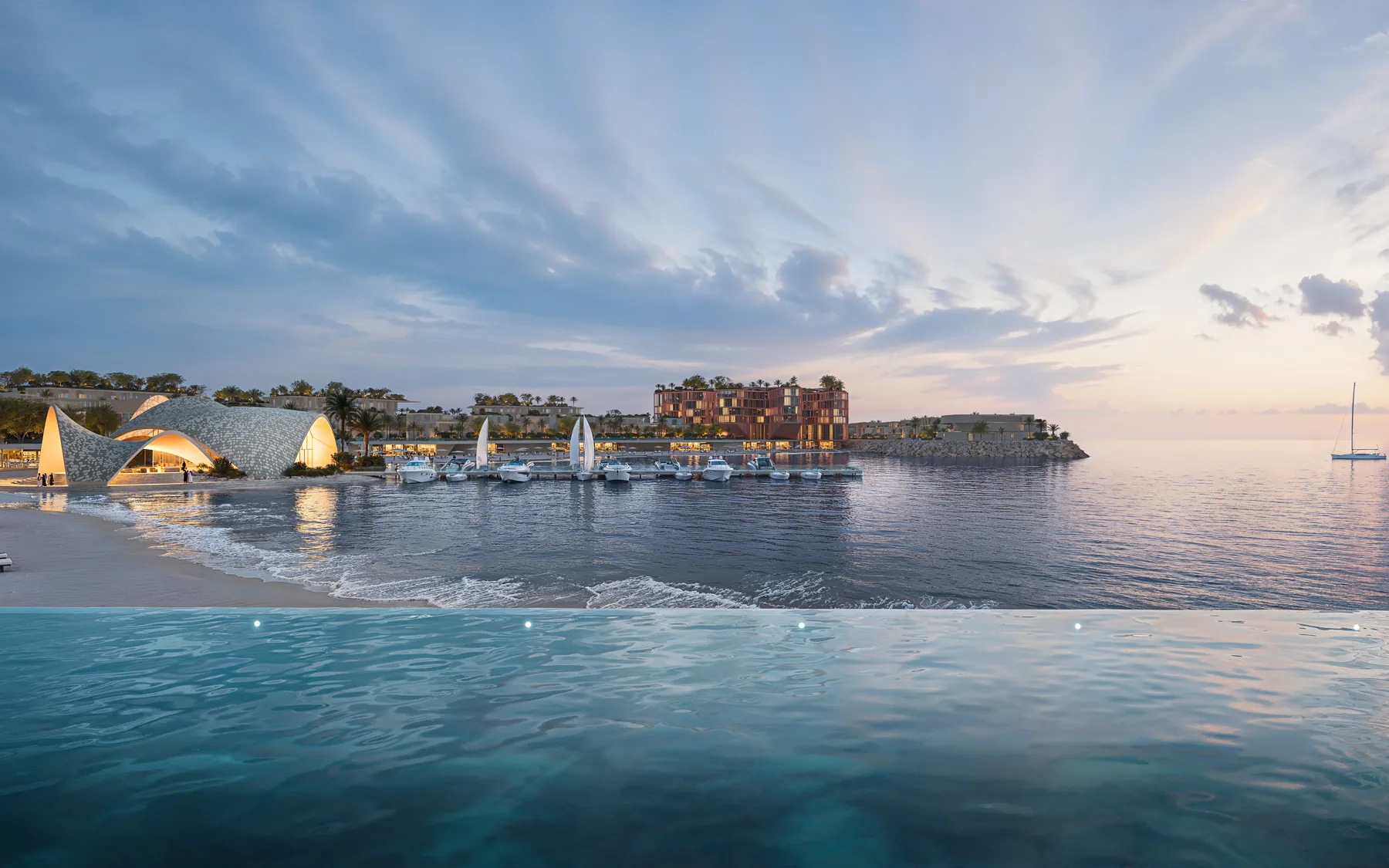 Mira Coral Bay lit at dusk beside the water, seen across an infinity pool with boats moored at the jetty